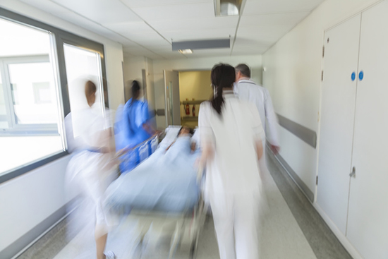 A motion blurred photograph of a child patient on stretcher or gurney being pushed at speed through a hospital corridor by doctors & nurses to an accident and emergency room